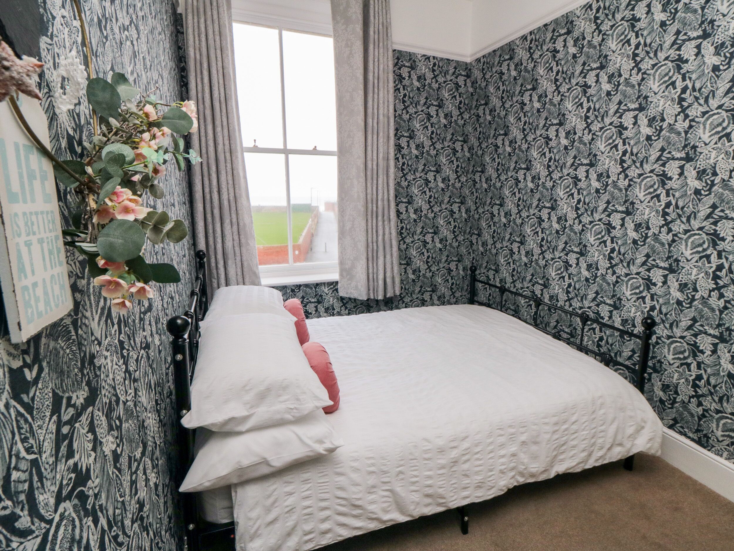Un dormitorio con una cama, un ventanal y un papel tapiz estampado.