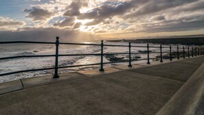 A coastal walkway with a metal railing, leading to the sea.