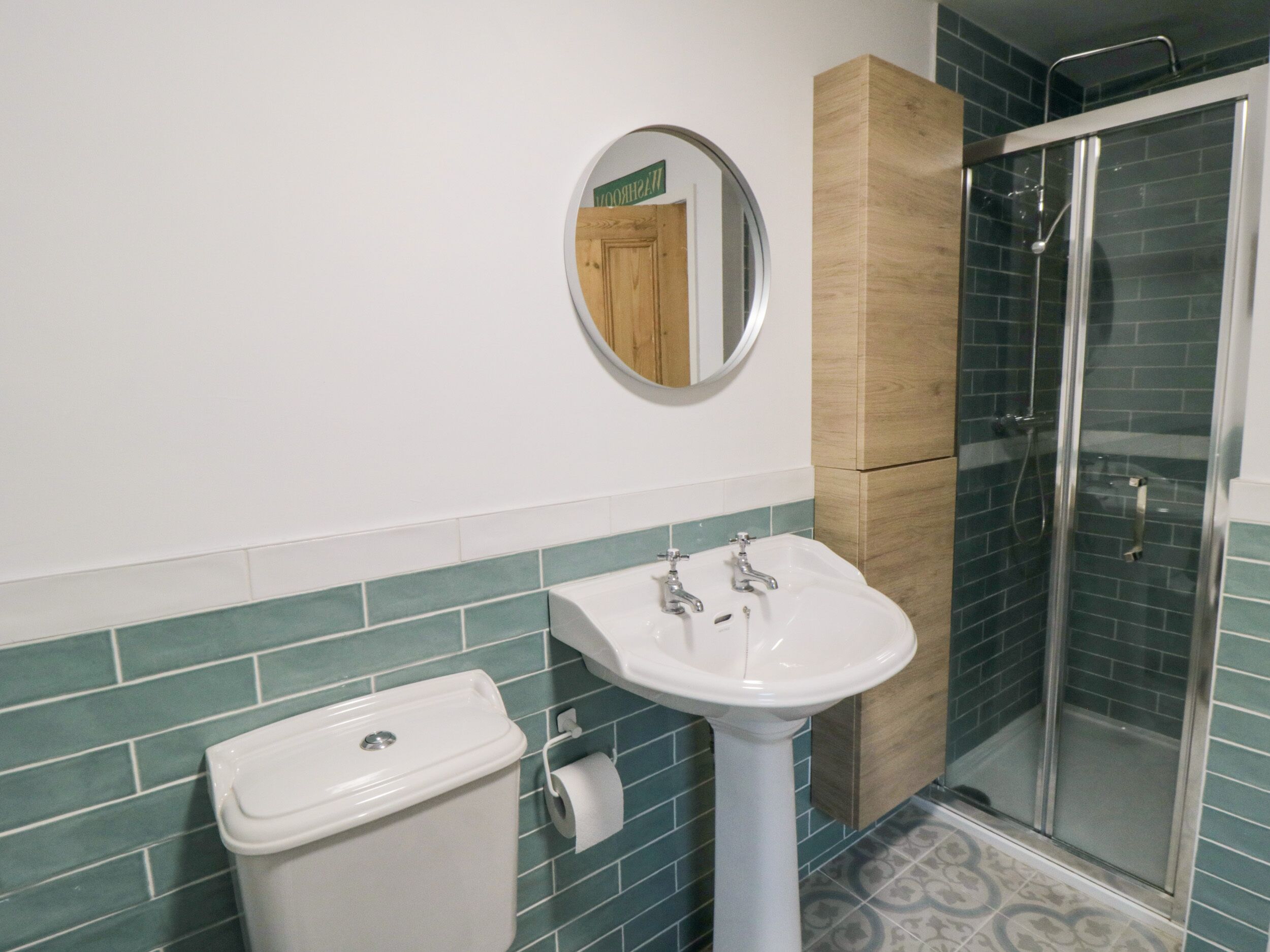 A bathroom with a white sink, a toilet, a mirror, and a shower enclosure.