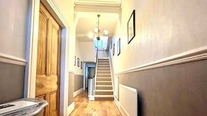 A hallway with wooden flooring, a staircase, and a radiator.