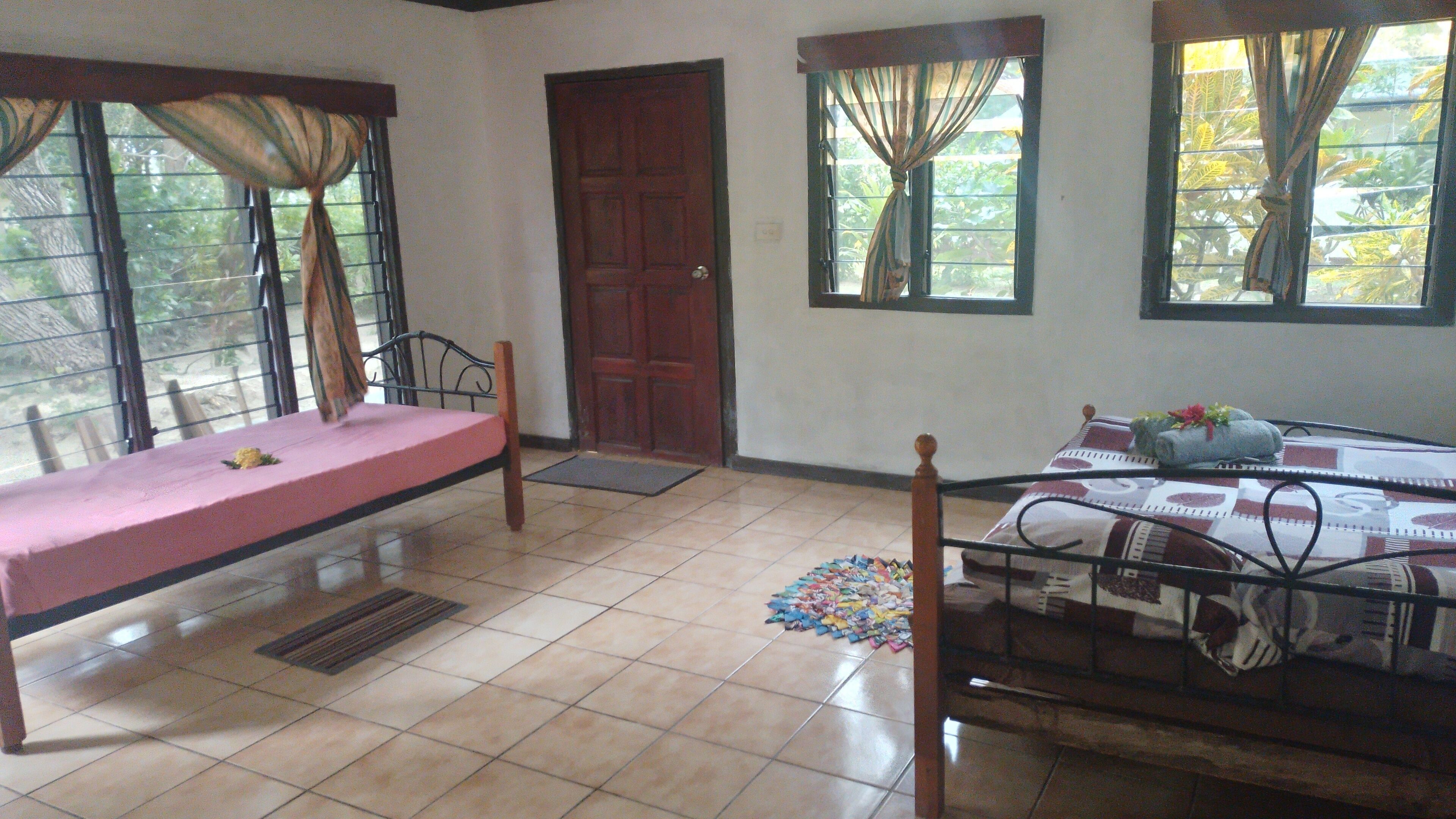 A room with two beds, a door, and windows with curtains.