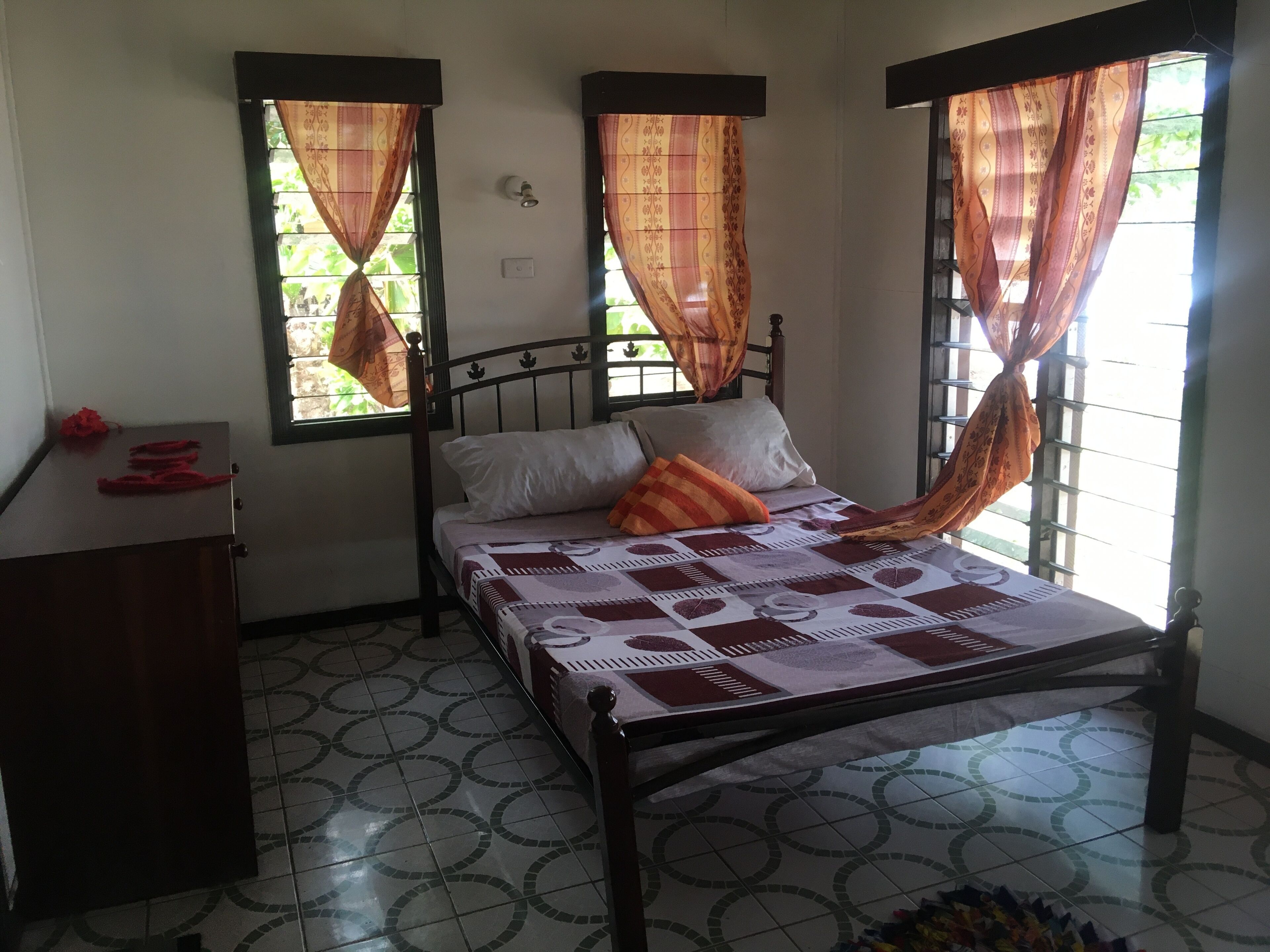 Un dormitorio con una cama, una mesita de noche y dos ventanas con cortinas.