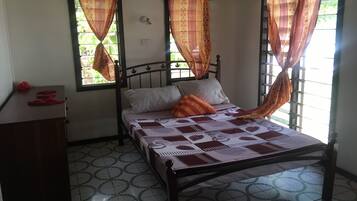 Un dormitorio con una cama, una mesita de noche y dos ventanas con cortinas.