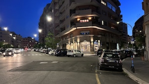 A multi-story building with a ground-floor commercial space, parked cars, and a pedestrian crossing.