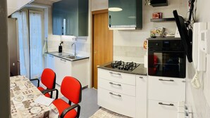 A compact kitchen with a gas stove, white cabinets, a sink, and a dining area with red chairs.