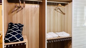 A wooden closet with a bench, hanging clothes, and folded towels.