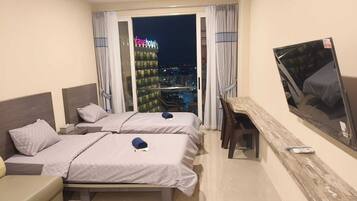 A hotel room with two beds, a desk, a chair, a TV, and a view of a cityscape at night.
