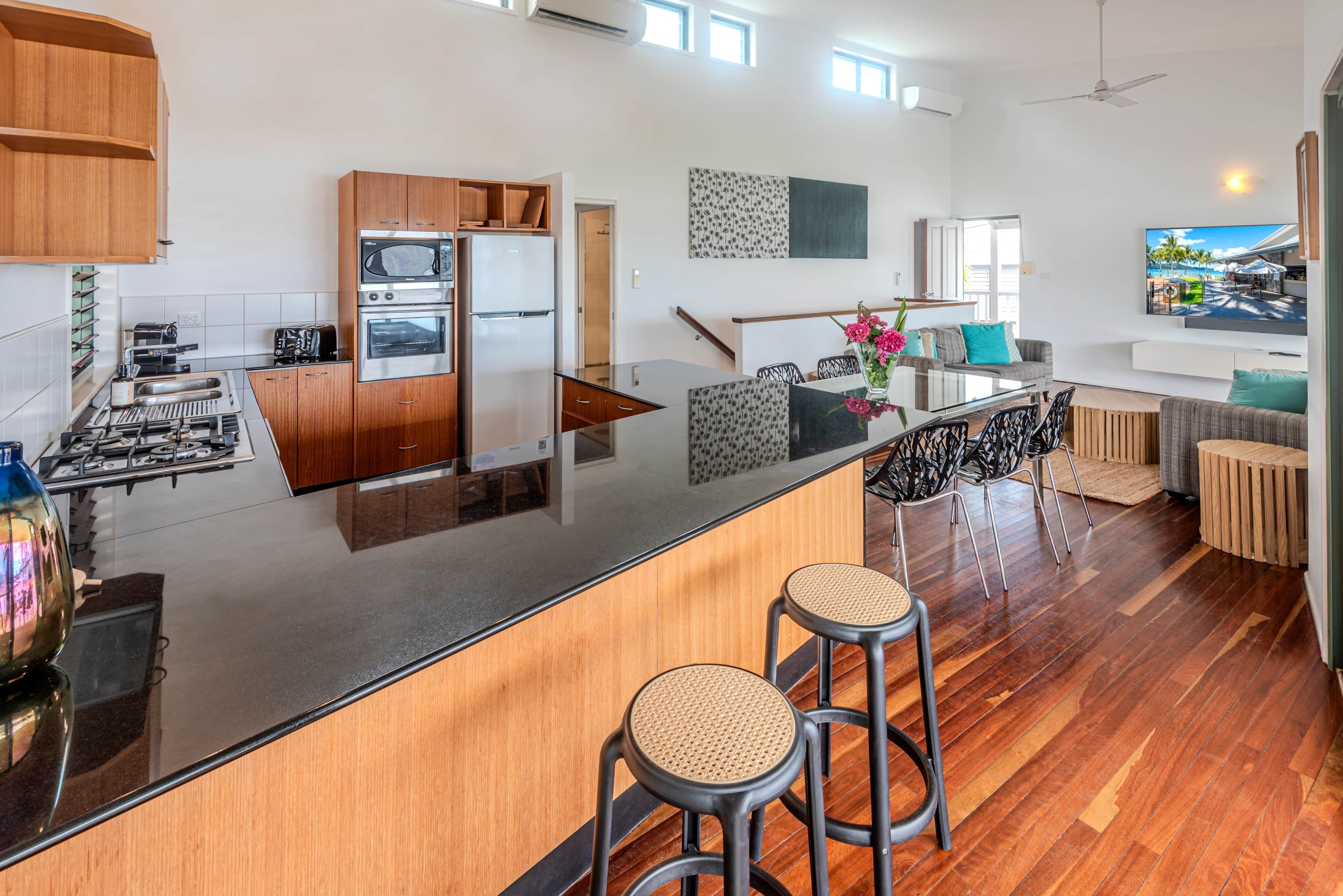 A modern kitchen with a central island, bar stools, and a dining area with a sofa and chairs.