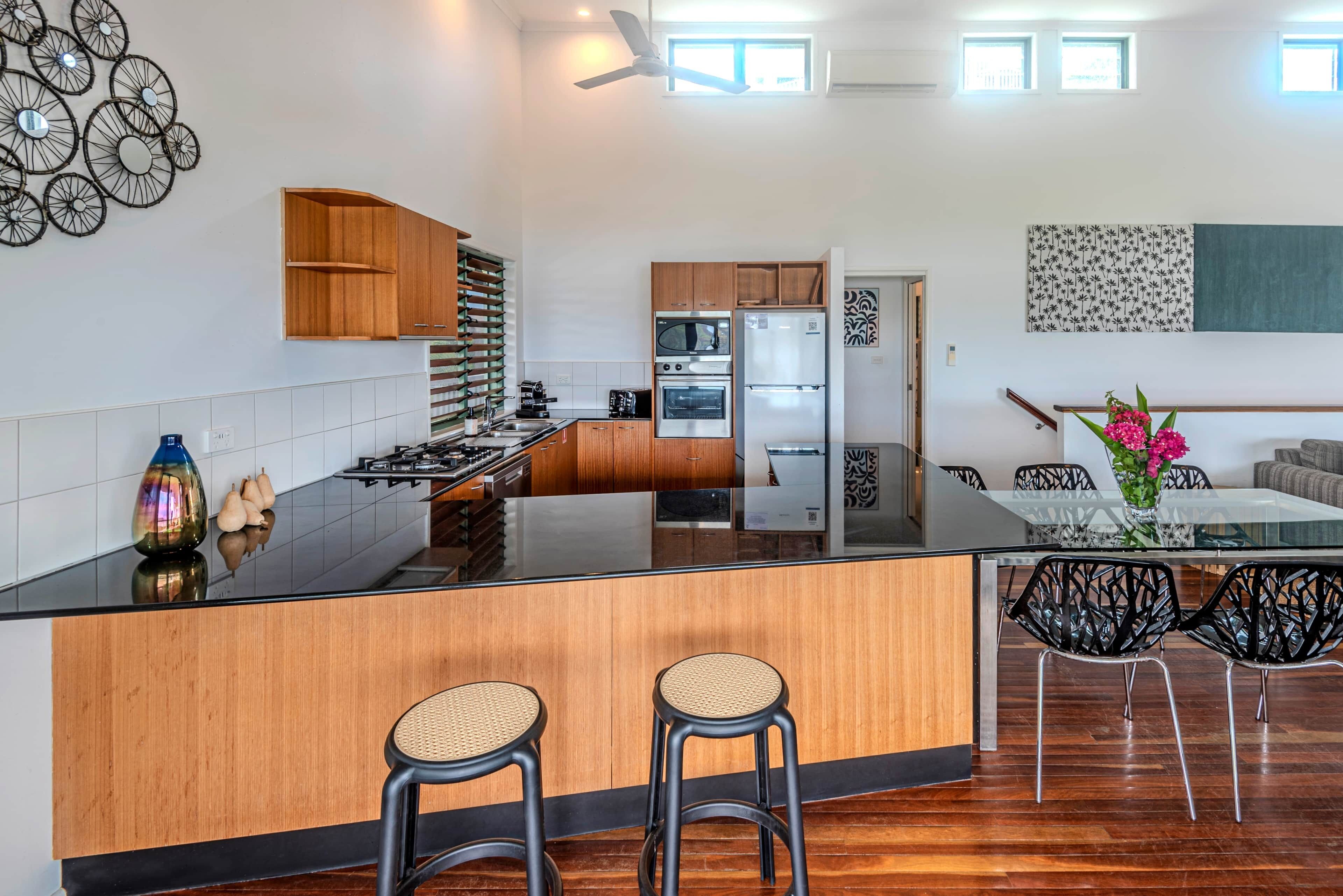 A modern kitchen with a central island, wooden cabinets, and a dining area with black chairs.