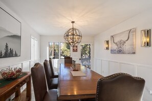 A dining room with a long wooden table, leather chairs, a chandelier, and artwork on the walls.