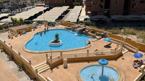 Une grande piscine extérieure dotée d’une fontaine centrale, entourée d’espaces de détente et d’une petite piscine circulaire.