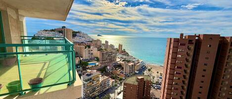 A high-rise building with a view of a coastal cityscape, including a beach and residential buildings.