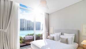 A modern hotel room with a large bed, a view of the city, and a balcony. - LUX The District One Lagoon View Suite (Dubai)