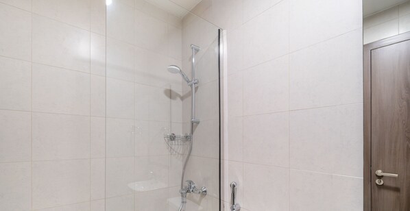 A shower with a handheld showerhead, a wall-mounted faucet, and a glass-enclosed shower area.
