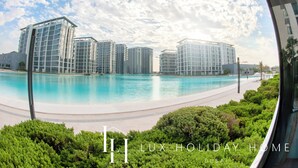 A modern hotel with a pool, surrounded by greenery and high-rise buildings. - LUX The District One Lagoon View Suite (Dubai)