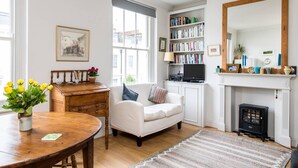 A living room with a fireplace, a bookshelf, a television, and a dining area with a table and chairs. - Delightful 1-bed, Pimlico (London)