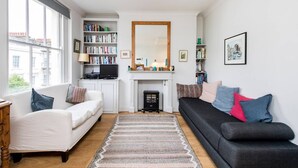 A living room with a fireplace, bookshelves, a television, and two sofas. - Delightful 1-bed, Pimlico (London)