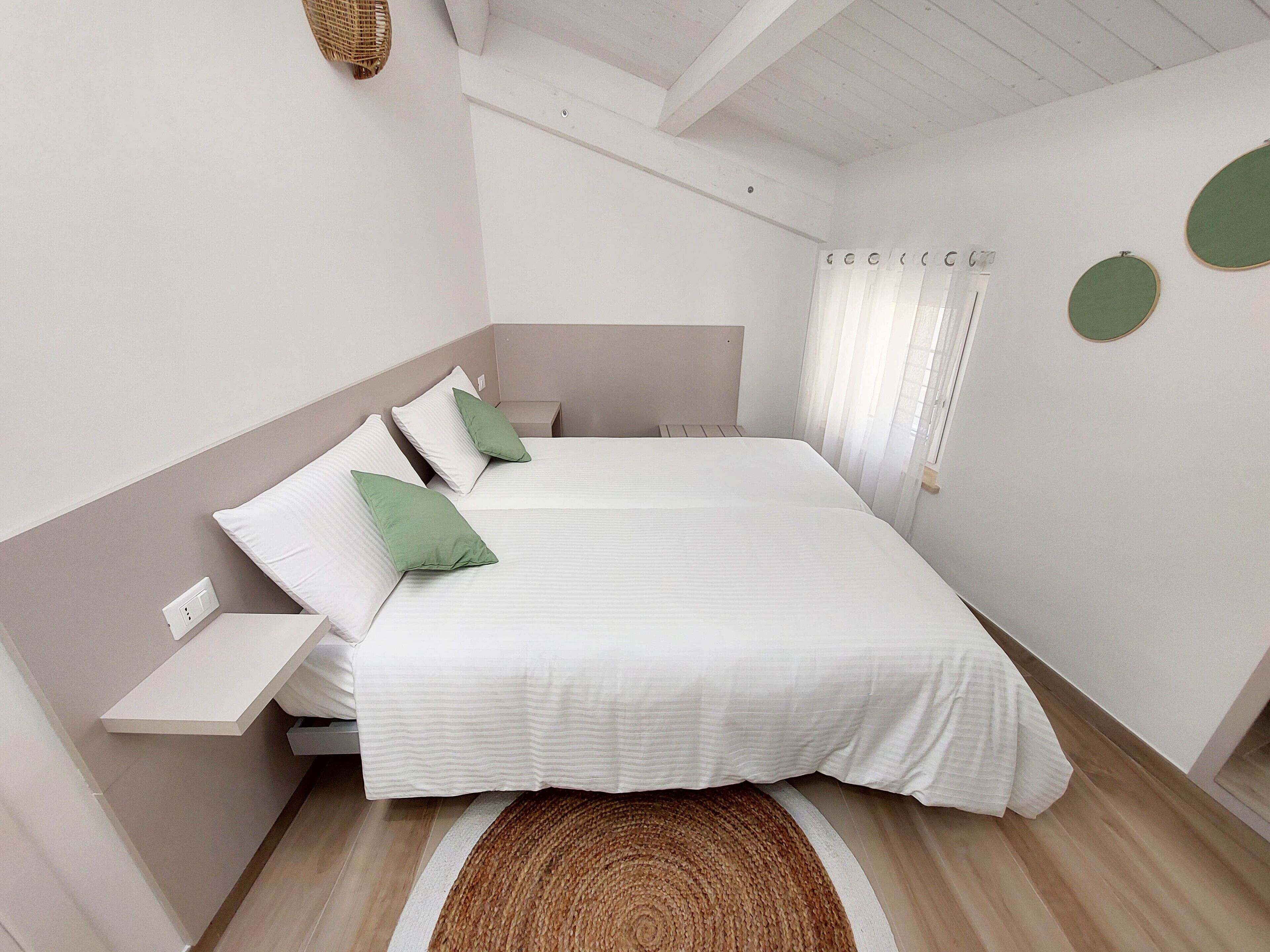 Un dormitorio con dos camas, una mesita de noche, un tapete tejido y una lámpara fijada a la pared.