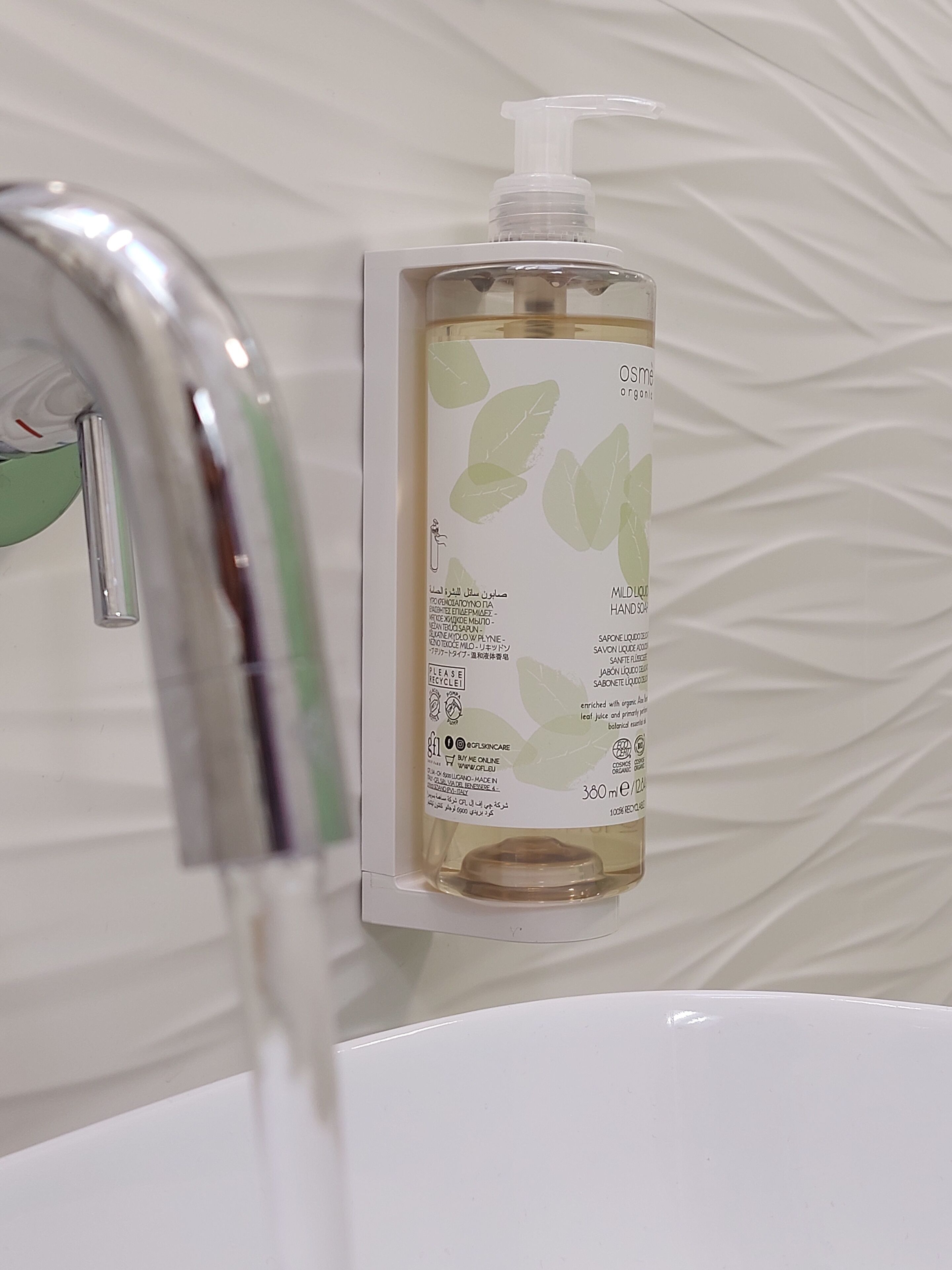 A bottle of organic hand soap with a pump dispenser, placed on a white sink with a faucet.