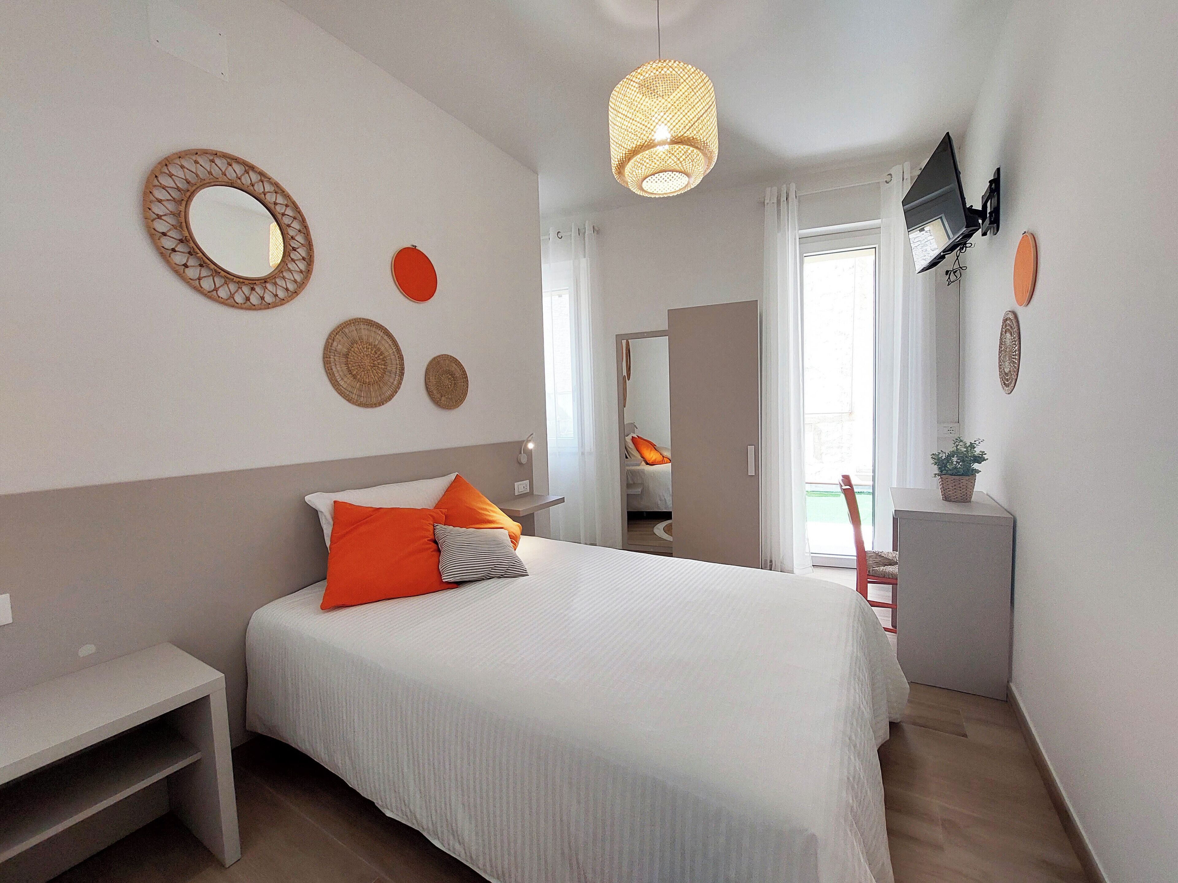 Een slaapkamer met een bed, nachtkastje, wanddecoratie en een aan de muur bevestigde televisie.