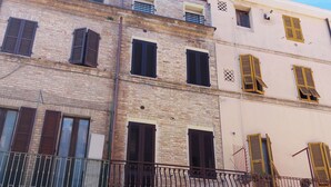 Un edificio de varios pisos con fachadas de ladrillo y enlucido, que presenta balcones con barandas de metal y diversos diseños de ventanas.