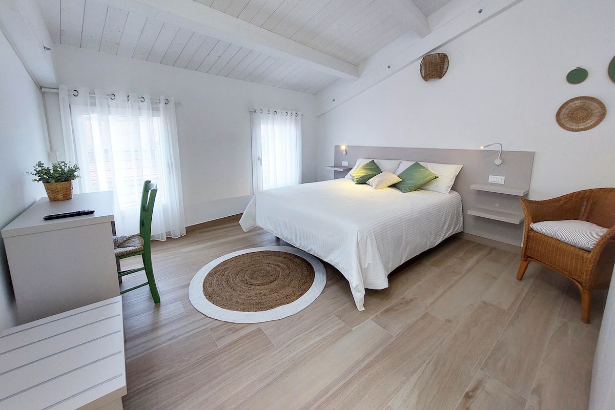 A bedroom with a bed, a chair, a desk, and a small table with a plant.
