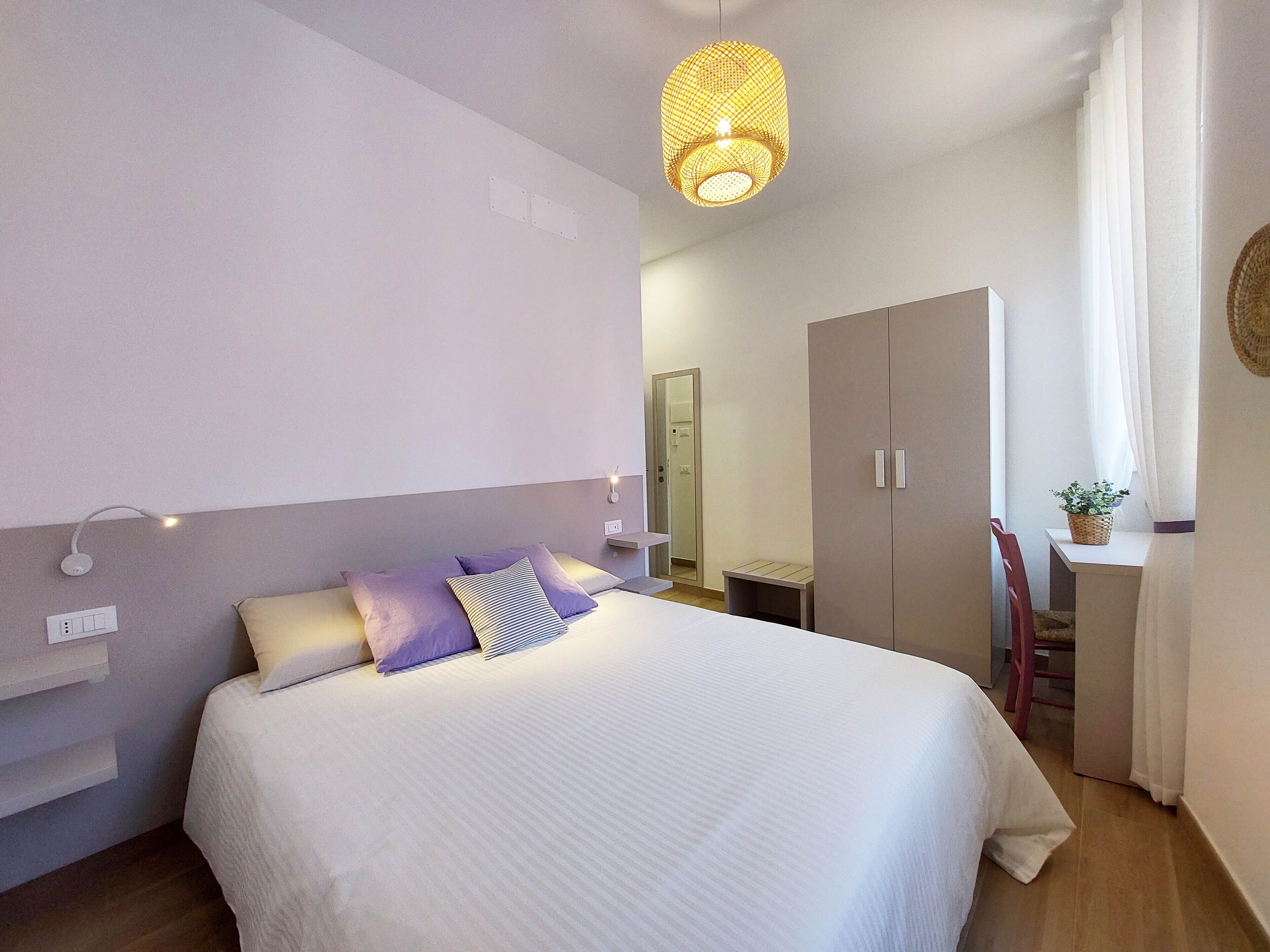 Une chambre à coucher comprenant un lit, une table de chevet, une armoire et un luminaire suspendu.