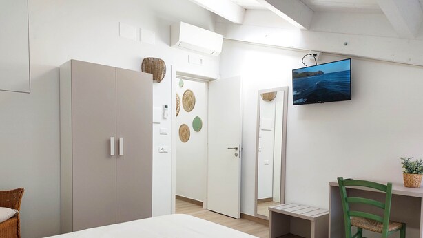 Un dormitorio con una cama, un escritorio y una silla. Hay un televisor montado en la pared.