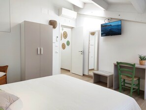 Ein Schlafzimmer mit Bett, Schreibtisch und Stuhl. An der Wand ist ein Fernseher angebracht.