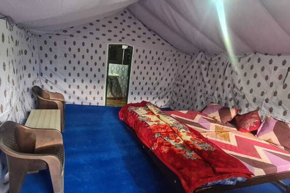 A tent-style room with a blue carpet, a bed with a red and patterned blanket, and a wooden chair.