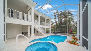 Una casa de dos pisos con piscina, un patio cubierto y vista a palmeras.