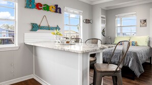 Quarto com ilha de mármore branco, cama com colcha cinza e parede com decoração de peixes e um letreiro 'Beach'.