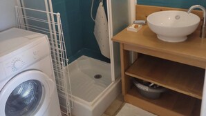 Un baño pequeño con lavadora, cabina de ducha y lavamanos con espejo.