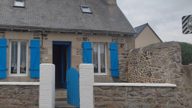 Un edificio de piedra con techo a dos aguas, puerta de madera y contraventanas azules.