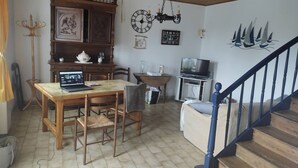 Un comedor con una mesa y sillas de madera, una computadora portátil sobre la mesa, una araña, un reloj y un televisor en la esquina.