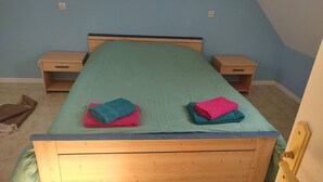 Habitación individual con una cama que tiene cabecera de madera, dos mesitas de noche y una colcha verde.