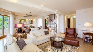 A spacious living room with a white sofa, a leather armchair, a glass coffee table, and a staircase leading to another level. - Beautiful home in Okrug Donji (Okrug Donji)