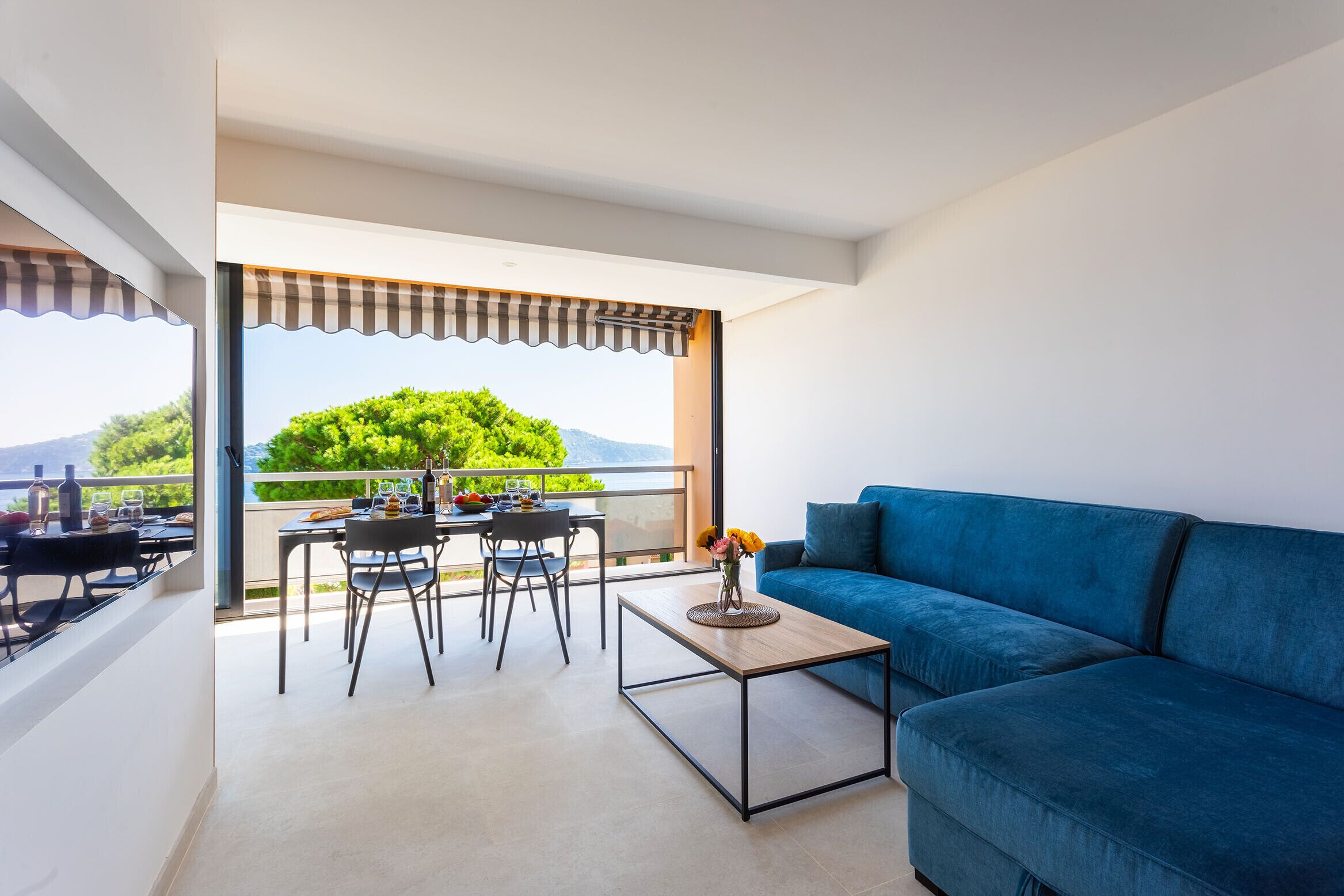 A balcony with a table and chairs, a blue sofa, and a view of greenery and mountains.