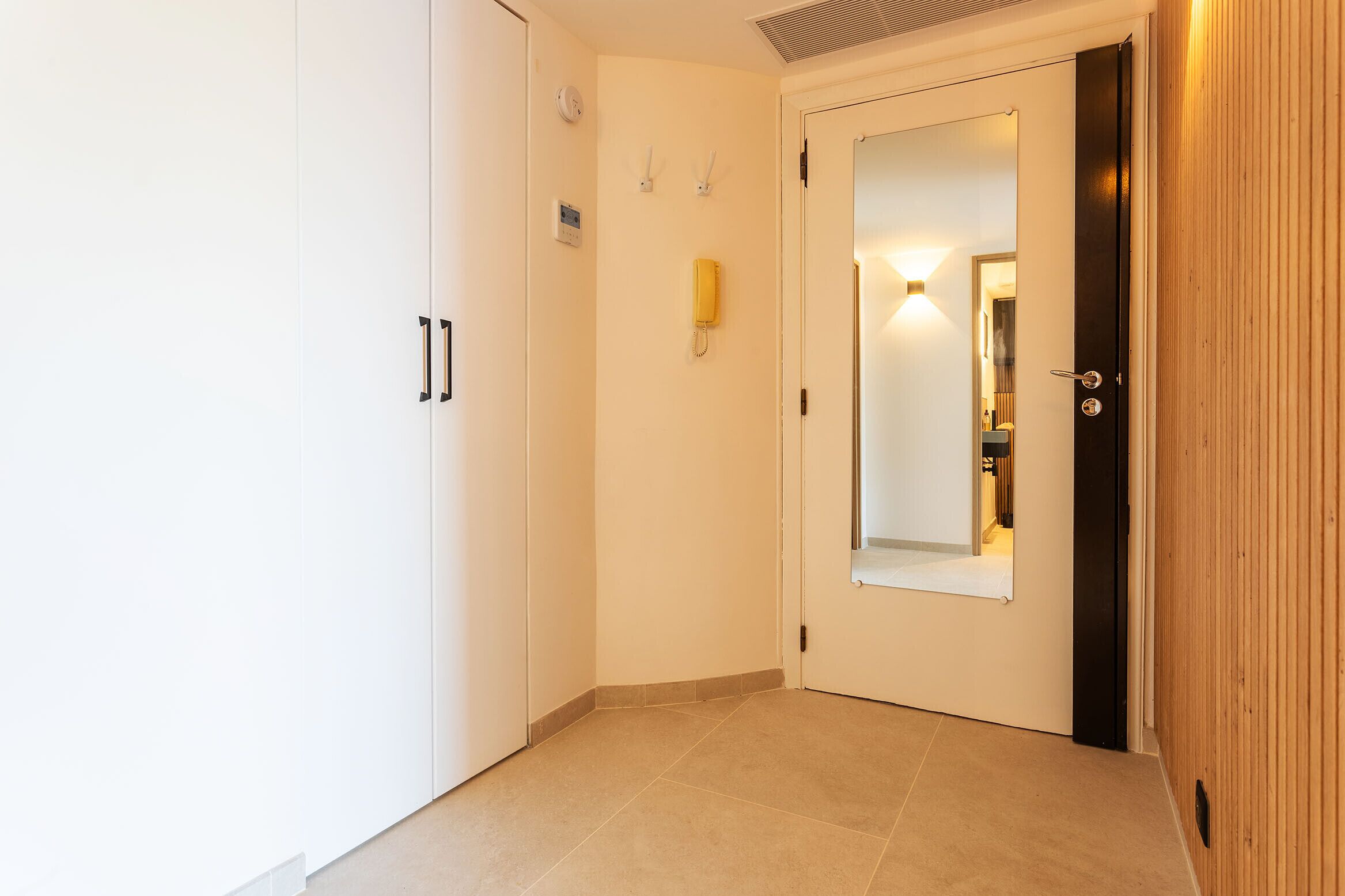 A hallway with a white door, a mirror, and a wall-mounted light fixture.