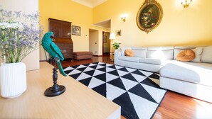 Un salon avec un canapé, un tapis à motifs, une table en bois et un perroquet perché sur un support.