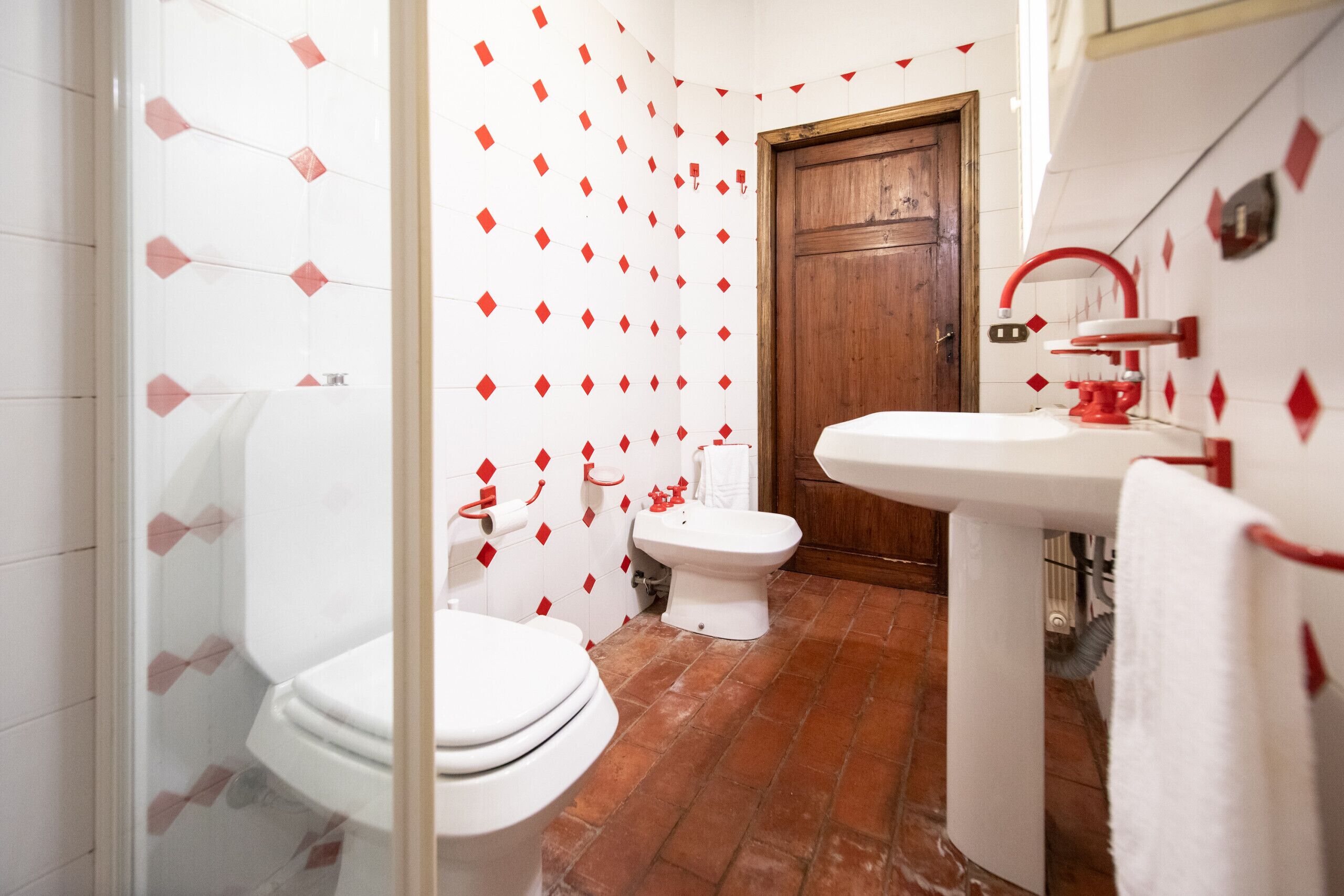 A bathroom with a white toilet, a bidet, and a sink with a red faucet.