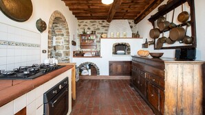 A rustic kitchen with a stone wall, wooden cabinets, a brick floor, and a traditional stove. - Villa Iris with Swimming Pool (Capannori)