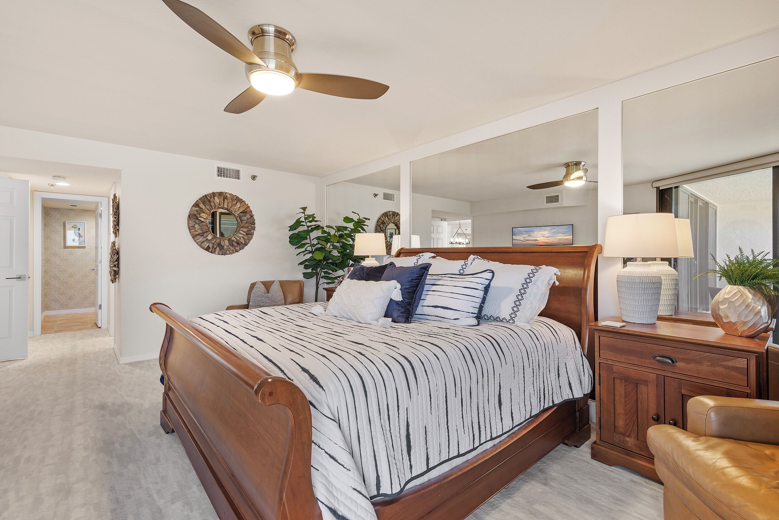 A bedroom with a wooden bed, a ceiling fan, a nightstand, and a mirror.
