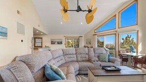 Ein geräumiges Wohnzimmer mit einem großen Ecksofa, einem Esstisch und einem Deckenventilator.