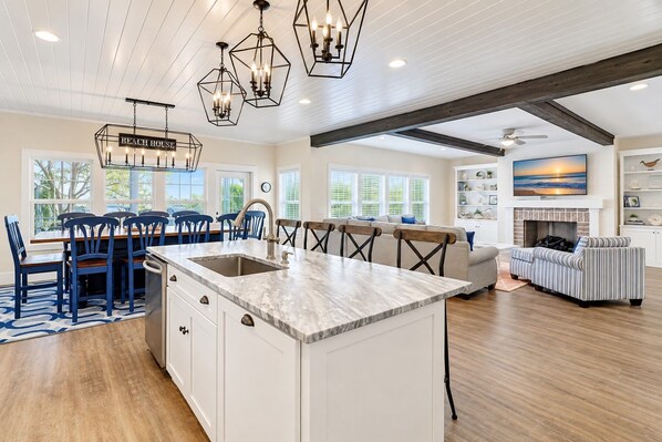 A spacious kitchen with a central island, a dining area with blue chairs, and a living room with a fireplace.