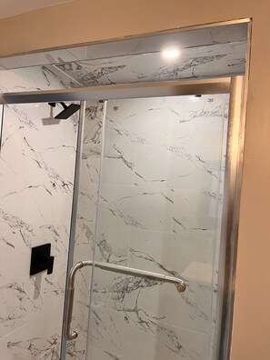 A glass-enclosed shower with marble tiles and a handrail.
