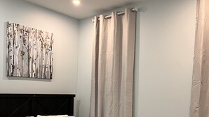 A bedroom with a bed, a headboard, a wall-mounted artwork, and a window with curtains. - One bedroom apartment/suite  (Whitby)