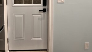 A white door with a window, a doorbell, and a light switch on the wall. - One bedroom apartment/suite  (Whitby)