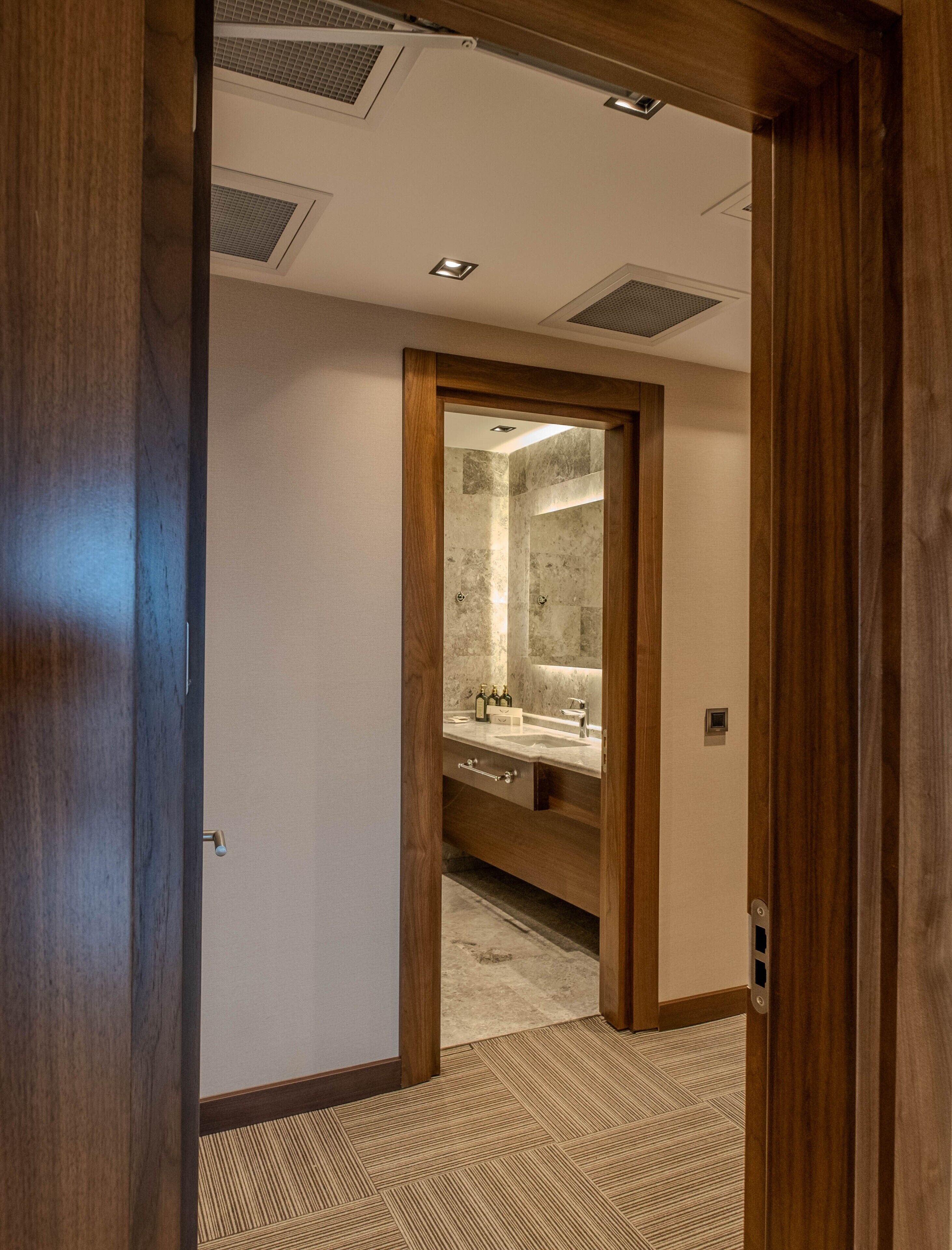 Ein Hotelzimmer mit Holztür, einem Badezimmer mit Marmorwaschbecken und Teppichboden.
