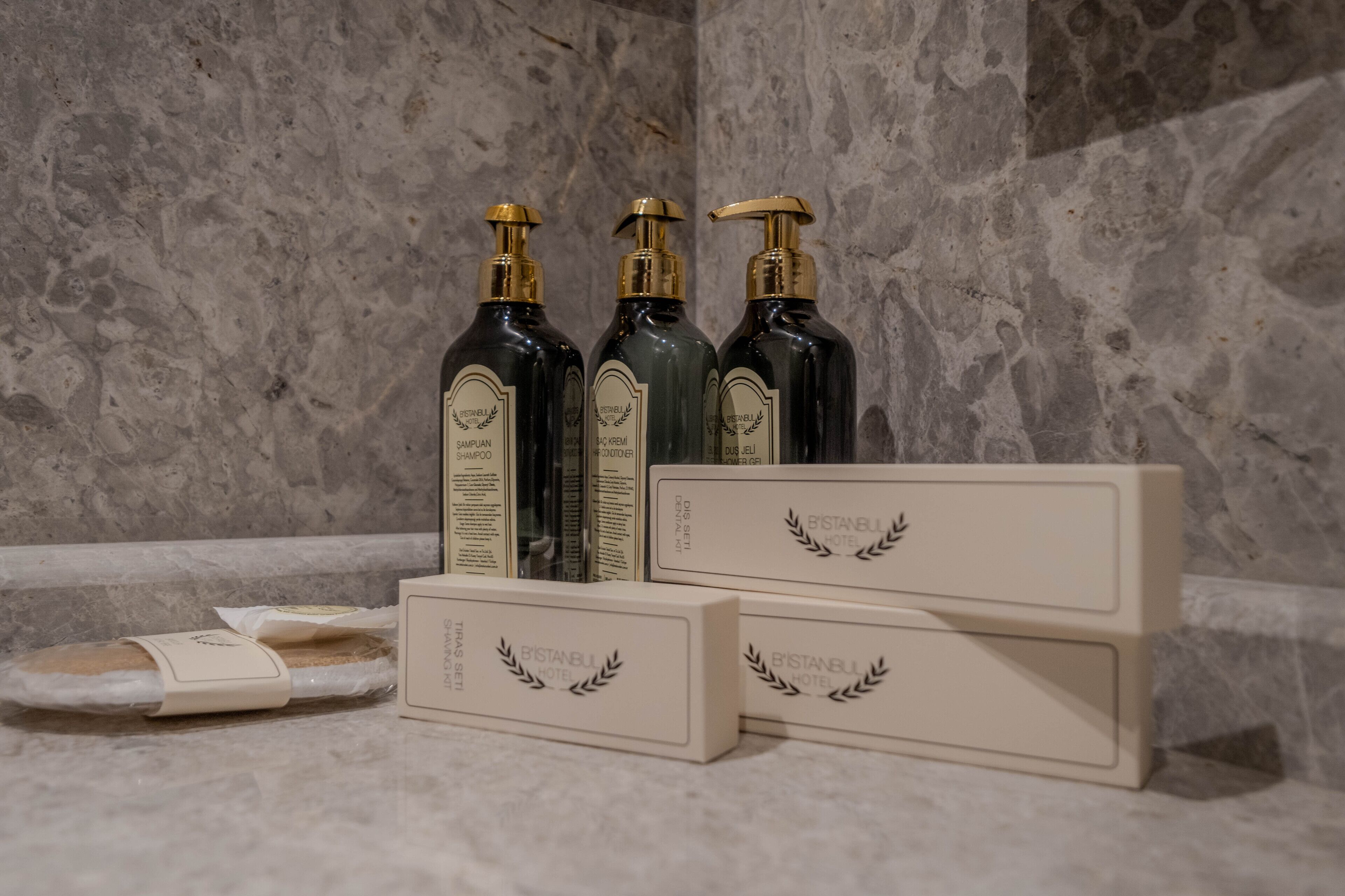 Tres botellas de champú y dos cajas con el logotipo de un laurel sobre una superficie de mármol.